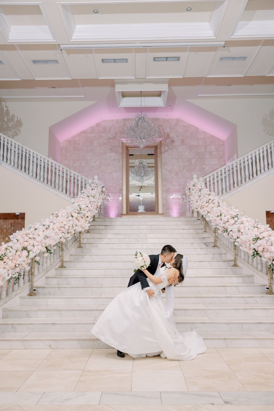 Groom dipping his bride for a kiss at the foot of a grand flower-lined staircase at Bellevue Conference Center, Chantilly VA — Kevin Socola Films