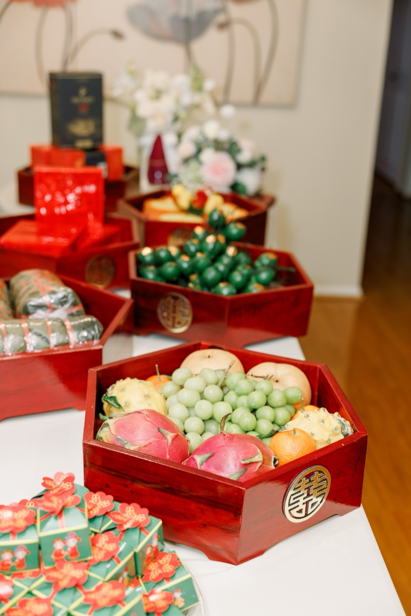 Vietnamese lễ ăn hỏi engagement ceremony — red lacquered mâm quả trays with dragon fruit, grapes, bánh phu thê pastries and double happiness 囍 symbol, photographed by Kevin Socola Films
