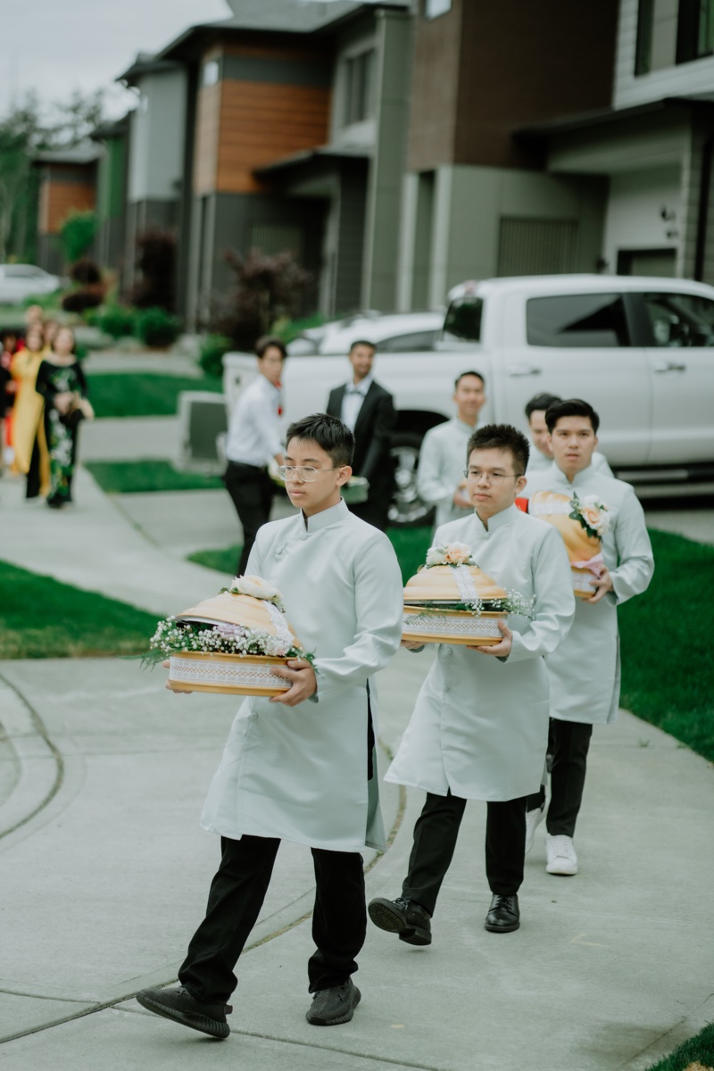 Vietnamese lễ rước dâu — groomsmen in traditional áo dài carrying red lacquered mâm quả betrothal trays during bride procession, photographed by Kevin Socola Films