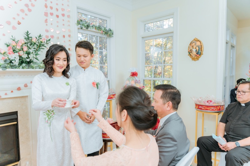 Vietnamese tea ceremony lễ dâng trà — bride and groom in white áo dài serving tea to seated parents and elders, photographed by Kevin Socola Films in the DMV